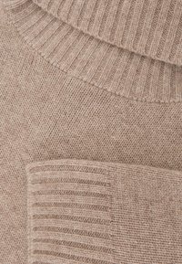 Béžový pletený sveter s jemnou textúrou, rebrovaným golierom a manžetami, a hladkým telom s jemnými farebnými odtieňmi.