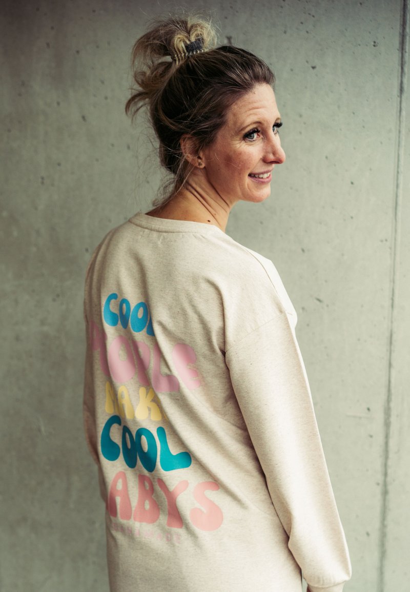 Beige Oversized-Sweatshirt mit buntem Text "COOL PEOPLE MAKE COOL BABYS" in Blau, Pink und Gelb, mit einer strukturierten Stoffoberfläche.