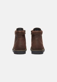 Stivaletti in pelle marrone con una superficie liscia, punta arrotondata e cerniere laterali. Sola in gomma nera resistente con leggera elevazione del tacco.