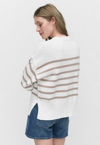 Witte gebreide trui met horizontale beige strepen, geribbelde zoom en zijsplitten; gecombineerd met denim shorts. Zachte textuur en een relaxte pasvorm.