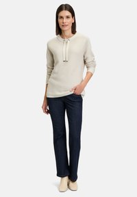 Beige gerippter Pullover mit rundem Halsausschnitt und Bindedetail, kombiniert mit dunkelblauen Schlagjeans und cremefarbenen Absatzstiefeln.
