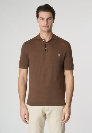 Polo shirt marrone a maniche corte con tessuto testurizzato, colletto a tre bottoni e un piccolo logo sul lato sinistro del torace. Abbinato a pantaloni di colore chiaro.