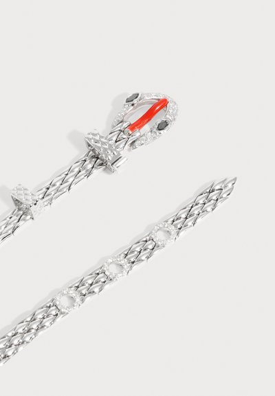 Ceinture tressée argentée avec une boucle texturée ornée de pierres noires et transparentes et un détail rouge en forme de langue sur fond blanc.
