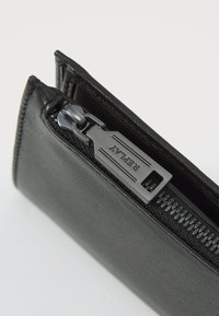 Billetera de cuero negro con un acabado texturizado, cremallera metálica con tirador y costuras finas a lo largo de los bordes.