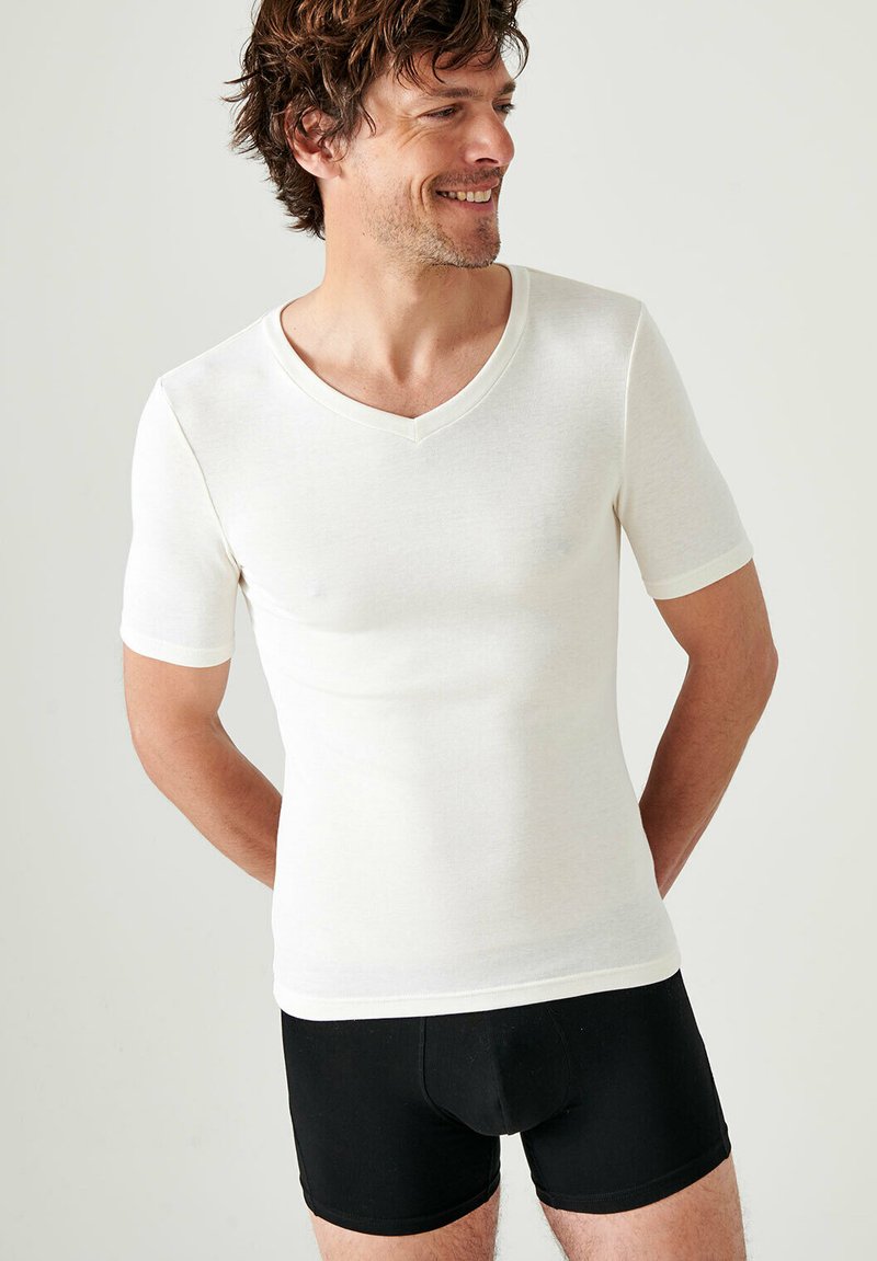 Witte fitted T-shirt met korte mouwen en V-hals, gemaakt van een gladde stof, gedragen met zwarte boxershorts.