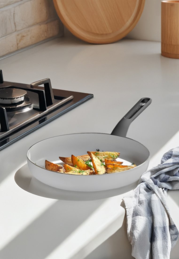 Sartén antiadherente blanca con un mango negro, que contiene verduras asadas en su interior, situada sobre una encimera de cocina clara.