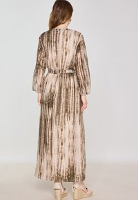 Abito maxi in tessuto leggero, presenta un motivo a strisce marroni e beige, maniche lunghe, vita rifinita con cintura e una silhouette fluente.