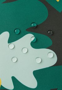 Tissu résistant à l'eau orné d'un motif abstrait de feuilles vertes et teal, avec de grosses gouttes d'eau reposant à la surface.