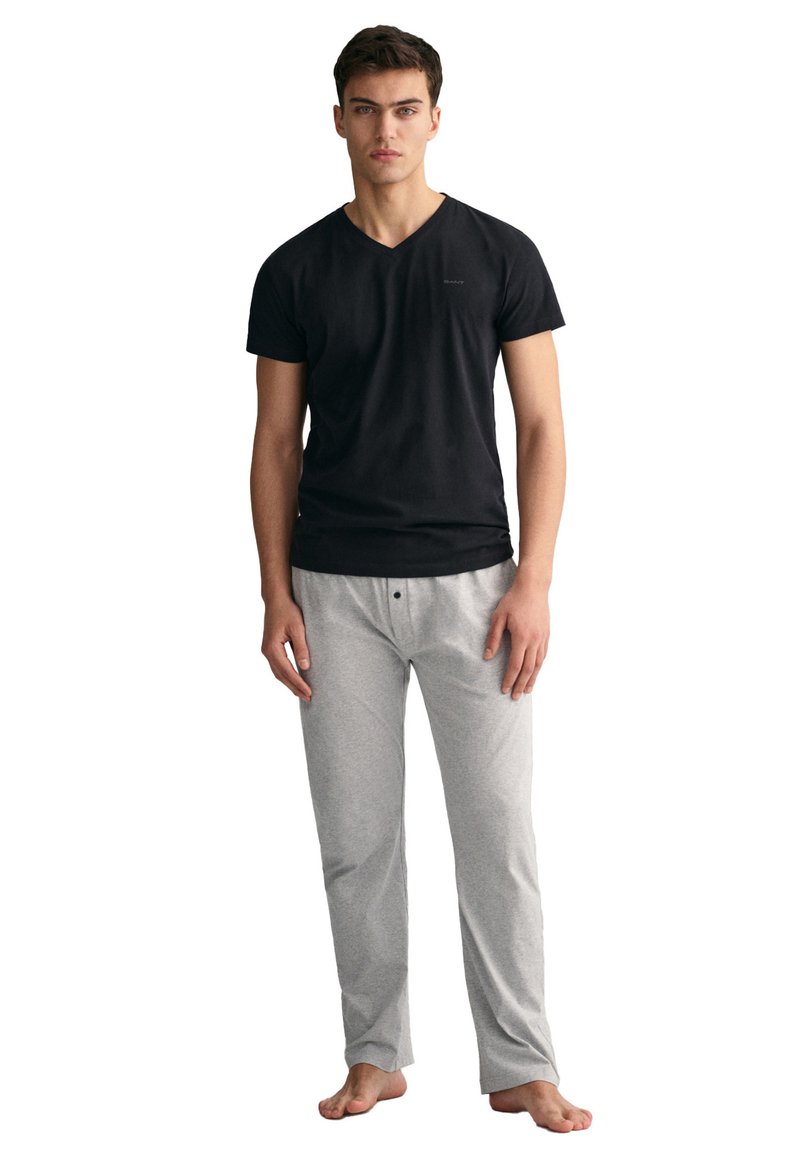 Schwarzes Baumwoll-V-Ausschnitt-T-Shirt kombiniert mit hellgrauen Baumwoll-Pyjama-Hosen mit durchgeknöpfter Front. Weiche Textur, lässige Passform.