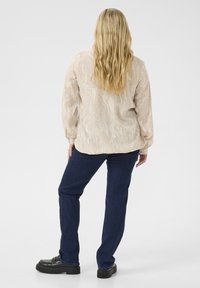 Beige dlouhý rukáv top s texturovaným, vlnitým vzorem, v kombinaci s tmavě modrými rovnými džíny a černými robustními botami.