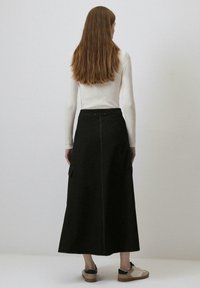 Long jupes en coton noir avec des poches latérales, taille haute et coutures contrastées. Portée avec un haut blanc ajusté et des baskets décontractées.