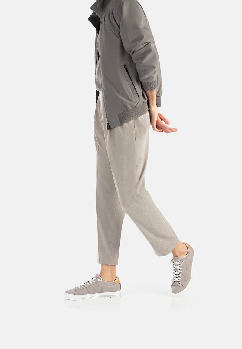 Graue Bomberjacke mit geripptem Saum, kombiniert mit hellgrauen tapered Pants und grauen Sneakers mit einem hellbraunen Absatz und weißer Sohle.