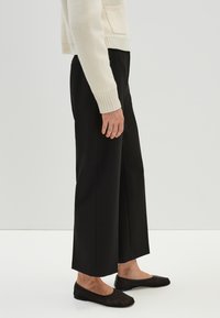 Zwarte wijde broek met een gladde textuur, voorzien van een hoge taille en een relaxte pasvorm. G gecombineerd met eenvoudige, zwarte ballerina's.