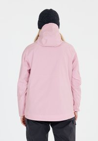 Helle pinke wasserfeste Jacke mit Kapuze, langen Ärmeln und lockerer Passform. Tragen über dunklen Hosen und zeigt ein minimalistisches Design.