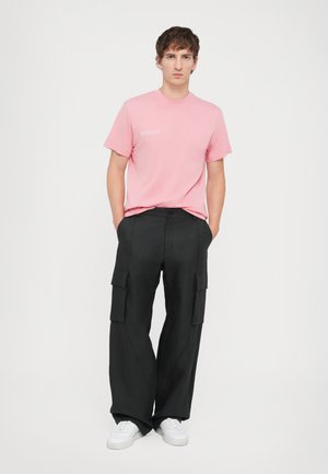 Lyserød bomulds-T-shirt med korte ærmer, parret med sorte haremsbukser med brede ben, der har sidelommer, og hvide sneakers.