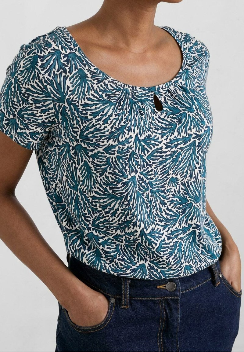 Kurzärmlige Bluse mit rundem Ausschnitt, mit blau-weißem Blattmuster. Hergestellt aus weichem Stoff, mit kleinem Schlüsselloch-Detail am Ausschnitt.