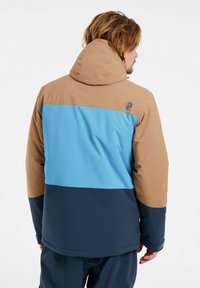 Chaqueta con bloques de color en secciones marrón, azul y marino. Diseño con capucha, textura suave y detalles cosidos. Logo en el hombro.