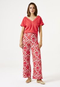 Rotes, gestricktes Oberteil mit V-Ausschnitt und aufgerollten Ärmeln, kombiniert mit weiten Hosen in Rot, Pink und weißen Blumenmustern.
