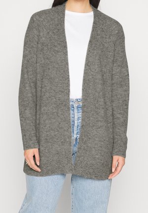 Kvinde iført en løs, grå, åben strikcardigan over en hvid t-shirt og lyseblå, højtaljede jeans.