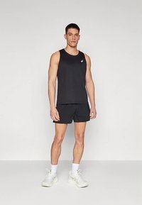 Débardeur et short de sport noirs, avec une texture lisse, un design minimaliste et un petit logo sur la poitrine. Portés avec des chaussettes blanches et des baskets.