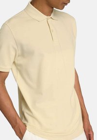 Polo shirt giallo chiaro realizzato in tessuto morbido, con colletto classico e due bottoni, dotato di maniche corte e taglio dritto.