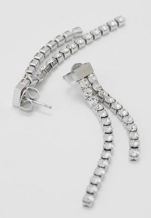 Boucles d'oreilles Guess ton argent avec deux rangées fines de cristaux ronds clairs et fermoirs papillon sur un fond clair.