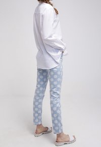 Vit långärmad skjorta, ljusblå byxor med prickar och vita sandaler utan häl. Tillverkad av bomull, avslappnad passform med synlig sömnad och fålldetaljer.