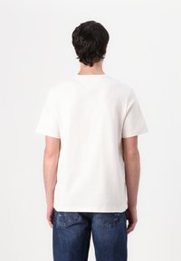 Short-sleeve, light beige t-shirt made of cotton, featuring a crew neckline and a straight hem, worn with blue denim jeans.