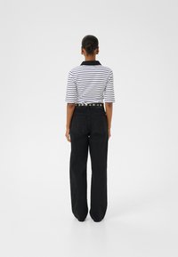 Svarta vida jeans parat med en svart och vit randig polo med krage. Noterbara detaljer inkluderar ett nitat bälte.
