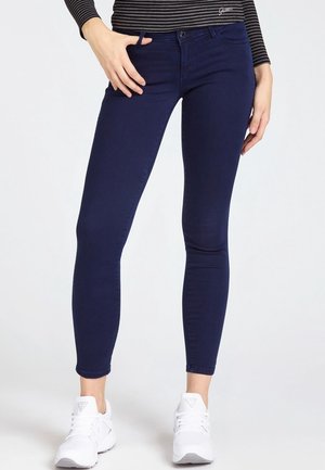 Slim-fit mørkeblå jeans båret med hvide sneakers og en langærmet top med sorte og grå striber.
