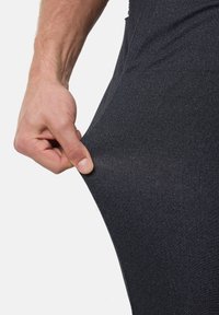 Mano pellizcando y estirando un tejido de pantalones ajustados de patrón de espiga oscuro, mostrando la elasticidad y textura de la tela.