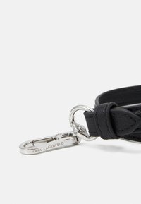 Czarny skórzany brelok z teksturowanym paskiem i srebrnym metalowym karabinkiem, z wygrawerowanym imieniem "KARL LAGERFELD."