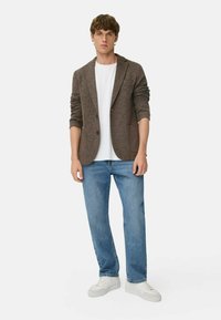 Brun tekstureret blazer med to frontlommer, parret med en hvid t-shirt, lyseblå jeans og hvide sneakers.