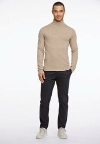 Suéter de cuello alto beige hecho de tela de punto, combinado con pantalones oscuros de color marino y zapatillas de color claro. Diseño ajustado con mangas largas.