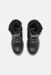 Botas de tobillo de cuero negro con un suave forro de piel de pelo, cordones plateados y una suela exterior texturizada en gris. Logo visible en el lado interno.