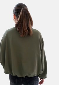 Olijfgroene oversized sweatshirt met een ronde zoom en verlaagde schouders, gemaakt van zacht stof. Gecombineerd met donkerdenim jeans.