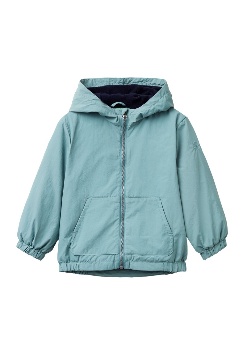 Světle modrá bunda s kapucí a předním zipem, elastickými manžetami, dvěma předními kapsami a tmavě modrou podšívkou. Měkká, voděodolná tkanina.