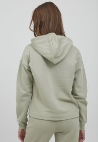 Világoszöld kapucnis felső, puha tapintással, kapuccsal és bordás mandzsettával. Egyszerű design, pamutból vagy hasonló anyagból készült.