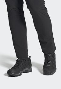 Zapatos de senderismo negros con parte superior texturizada, diseño con cordones y cierre de ajuste rápido, y suela resistente para tracción. Adecuados para uso al aire libre.