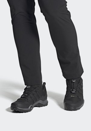 Zapatos de senderismo negros con parte superior texturizada, diseño con cordones y cierre de ajuste rápido, y suela resistente para tracción. Adecuados para uso al aire libre.