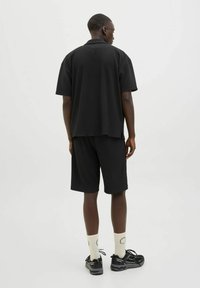Black short-sleeve shirt with a ribbed texture paired with matching shorts. Worn with black sneakers and cream-colored socks.