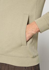 Lichtgroene sweatshirt met gestructureerde stof, voorzien van een zijzak en geribbelde manchetten. Het ontwerp is eenvoudig en nauwsluitend.