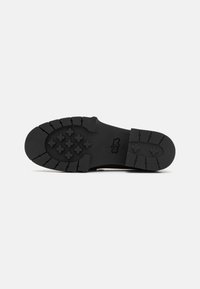 Black rubber shoe sole with textured tread design, featuring ridges and cross patterns for enhanced grip and durability. Size 8.5 noted.