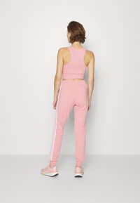 Rosa sportlicher Cropped-Top und passende Jogginghose mit weißen Seitenstreifen. Das Material ist glatt und elastisch. Die Schuhe sind hellrosa mit einer weißen Sohle.