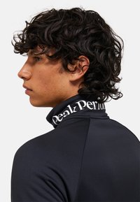 Maglione nero a collo alto con texture liscia; presenta un logo bianco sul colletto. Design aderente, che enfatizza una silhouette affusolata.