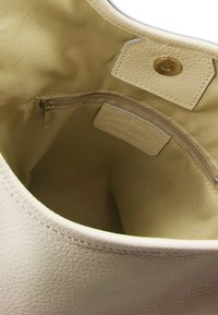 Witte leren handtas met een gladde textuur, voorzien van een beige binnenvoering en een ritszak. Cirkelvormig met gestikte randen.