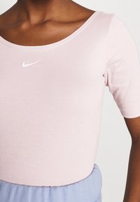 Light pink fitted T-shirt with a wide neckline, short sleeves, and a small white Nike logo on the chest, made of soft cotton material.