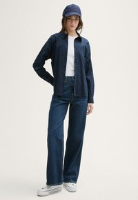 Navy long-sleeve shirt with button front, cotton fabric, and light pattern; paired with high-waisted dark denim jeans and white sneakers.