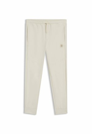 Helle beige Jogginghose aus weichem Material mit elastischem Bund, seitlichen Taschen und einem kleinen Logo-Aufnäher auf der Vorderseite.