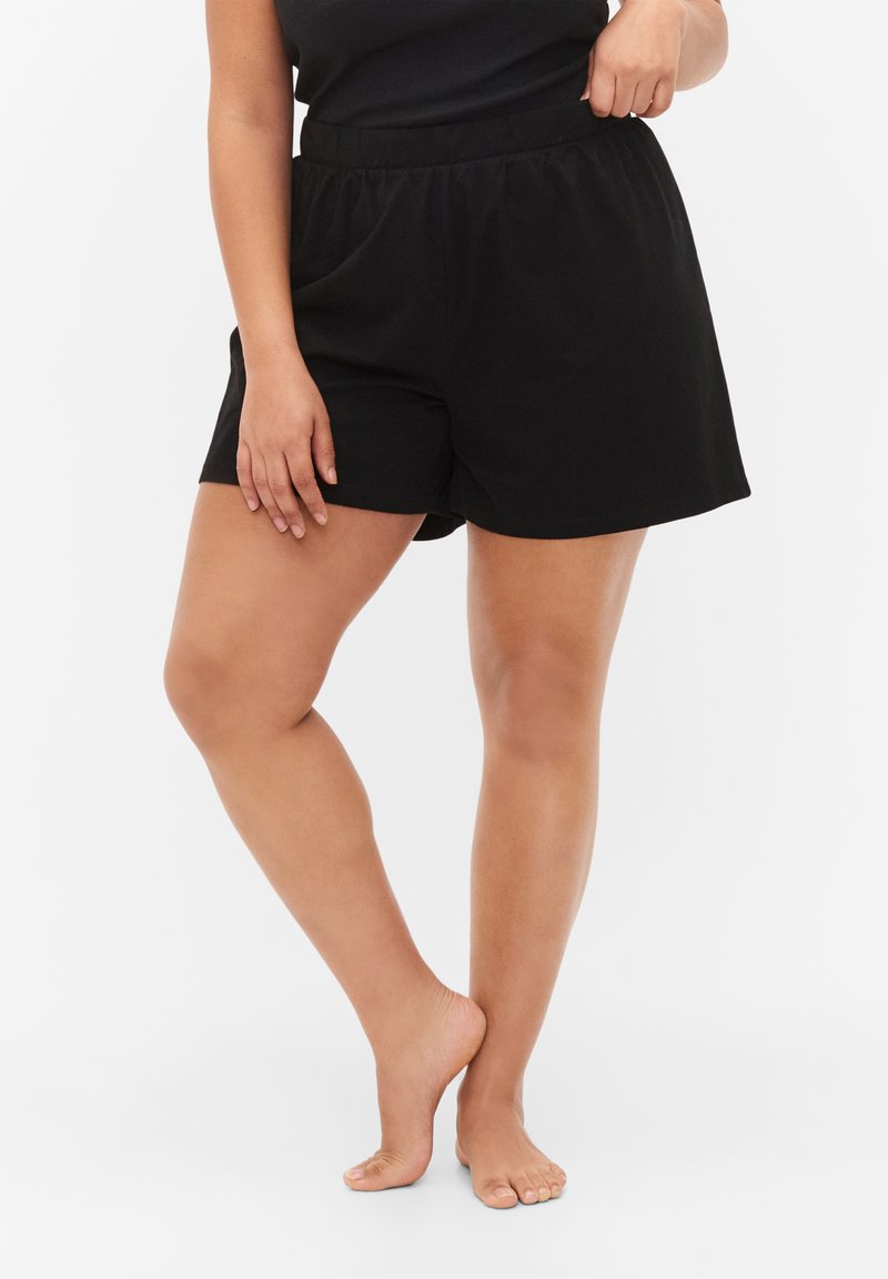 Zwarte katoenen shorts met een elastische tailleband, een ruime pasvorm en zijzakken, gepresenteerd op een lichte achtergrond.